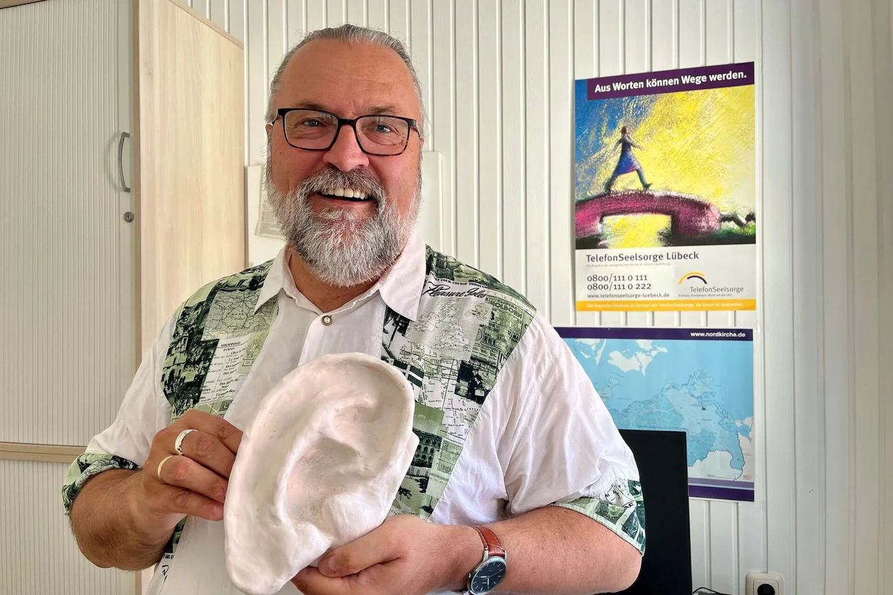 Mann steht mit Gipsohr in der Hand da und lächelt in die Kamera.