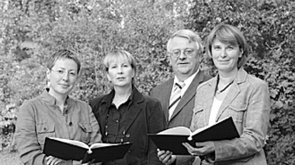 Vier Personen, drei Frauen, ein Mann stehen nebeneinander, links und rechts halten die Damen jeweils eine offene schwarze Mappe in den Händen
