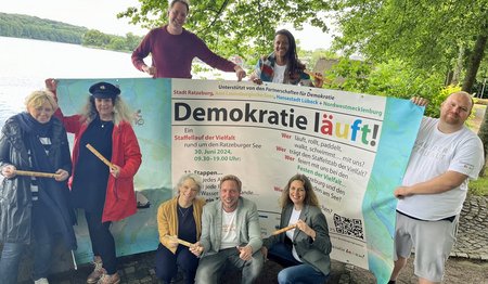 Eine Gruppe Menschen steht mit einem großen Plakat an einem See.