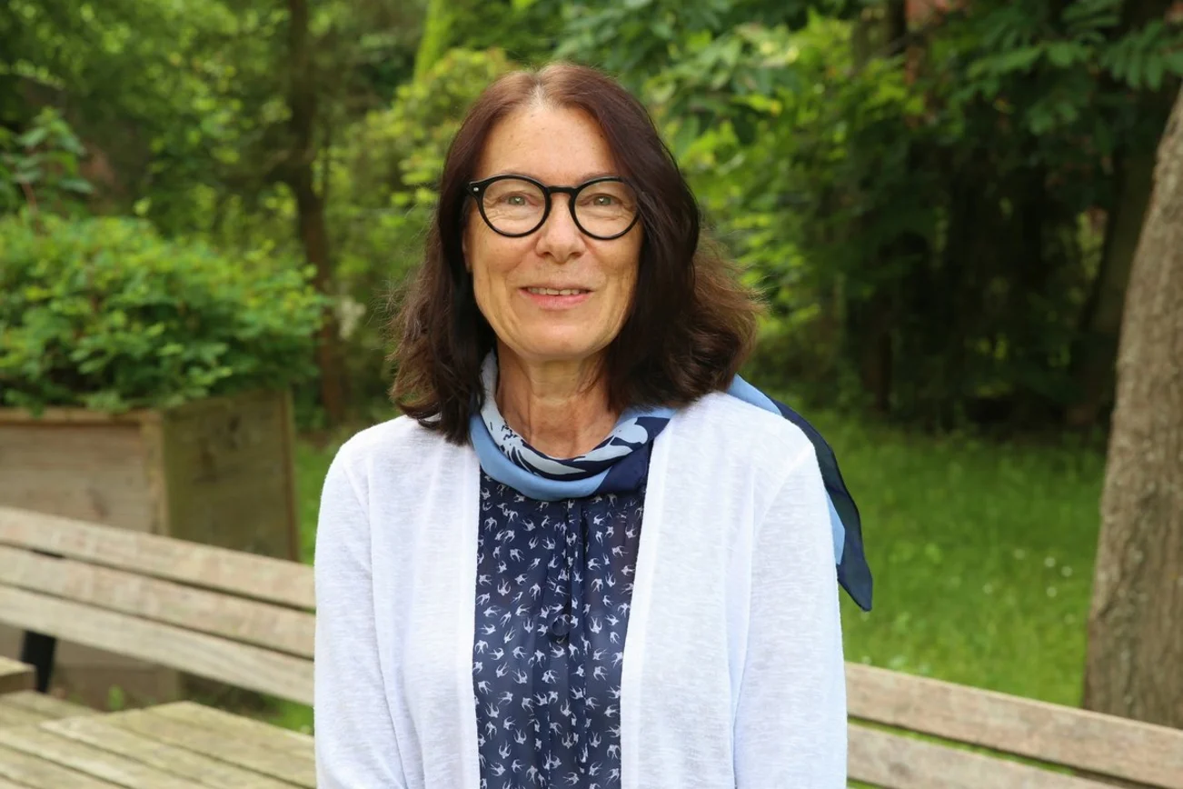 Eine Frau mit dunklen langen Haaren und Brille lächelt in die Kamera.