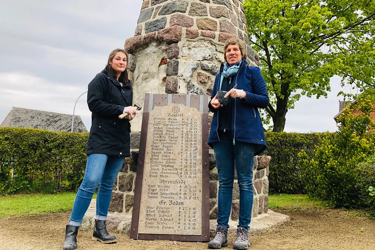 Malaika Krohn (re.) restauriert mit Theda Meierhöns das Ehrendenkmal. Stehend die gesicherte Platte, die in mehrere Teile zerbrach.