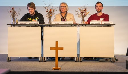 Das neue gewählte Synodenpräsidium aus drei Personen sitzt hinter einem großen Tisch.