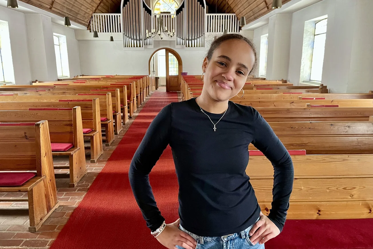 Junge Frau steht in einer Kirche und lächelt in die Kamera.