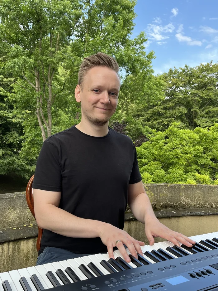 Ein junger Mann sitzt draußen im Grünen an einem Piano.
