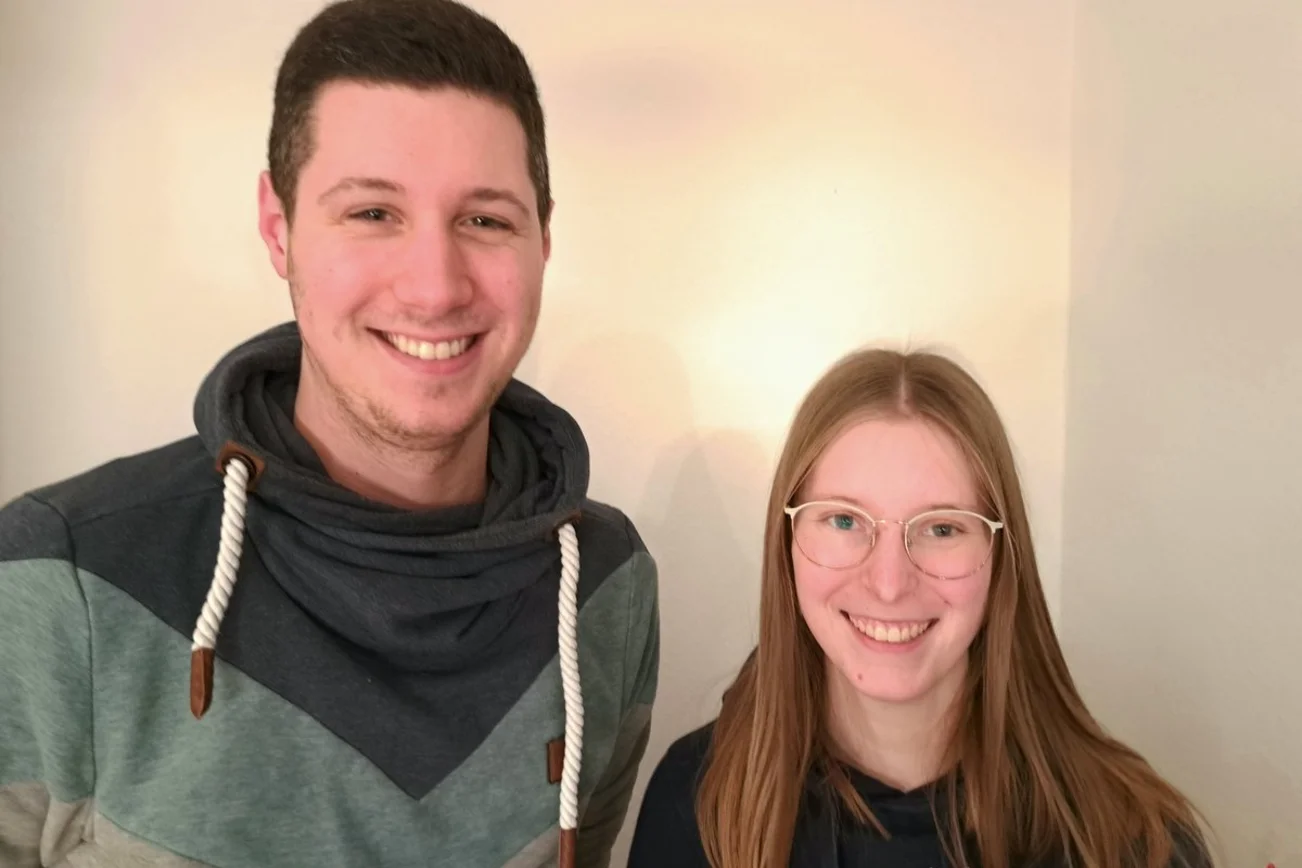 Zwei Menschen lächeln in die Kamera. 