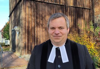 Ein Pastor steht vor einer Kirche - Copyright: KKLL