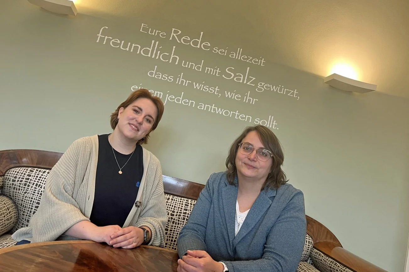 Zwei Frauen sitzen auf einem Sofa und lächeln in die Kamera.