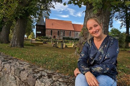 Eine Frau sitzt auf einer Mauer vor einer Kirche. - Copyright: Oliver Pries