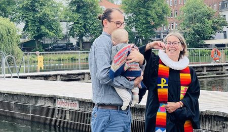 Der kleine Ferdinand verschläft seine Taufe in den Armen von Papa Christoph Unglaub. Rechts Pastorin Nicola Nehmzow.