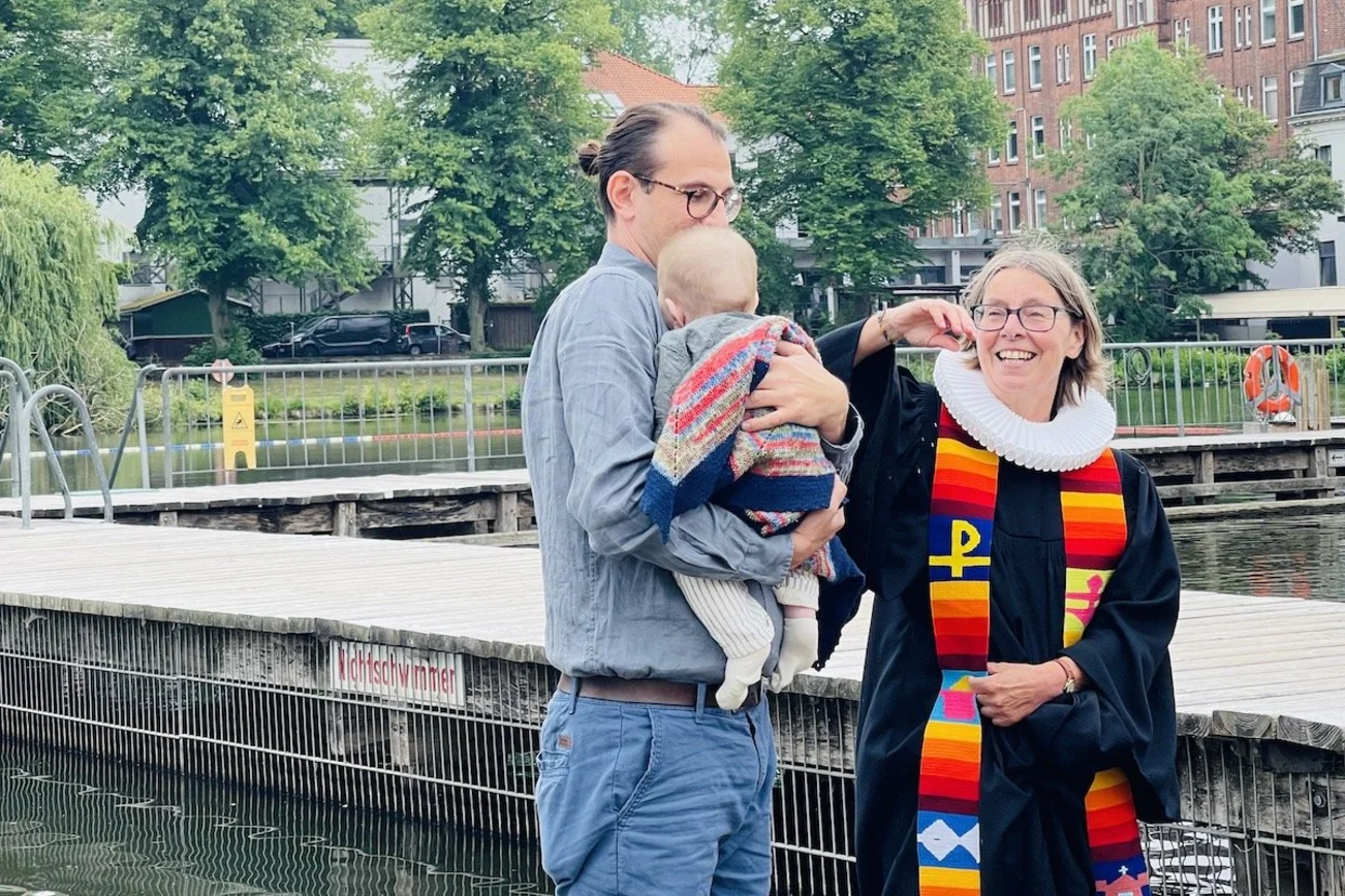 Der kleine Ferdinand verschläft seine Taufe in den Armen von Papa Christoph Unglaub. Rechts Pastorin Nicola Nehmzow.