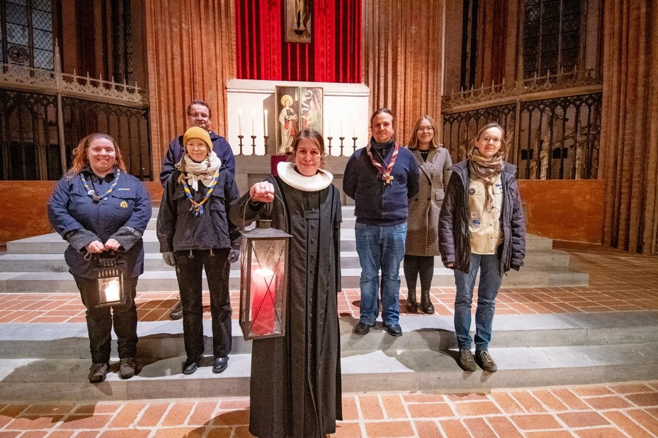 Mehrere Personen stehen in einer Kirche und halten eine Laterne mit einer brennenden Kerze. 
