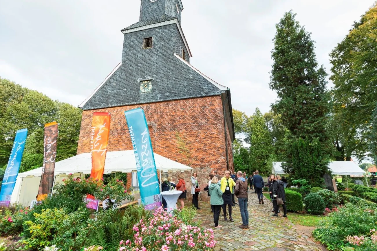 Eine Kirche, Menschen vor der Kirche, Fahnen und ein Pagodenzelt.