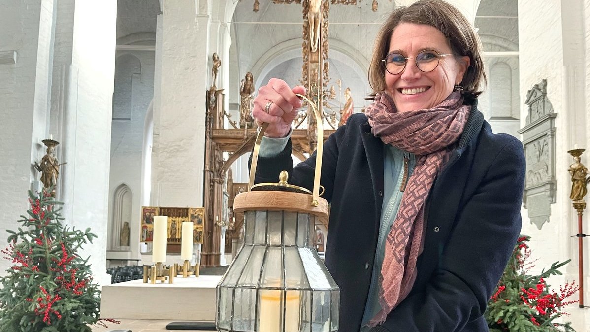Eine Frau steht mit einem Windlicht in einer Kirche. 
