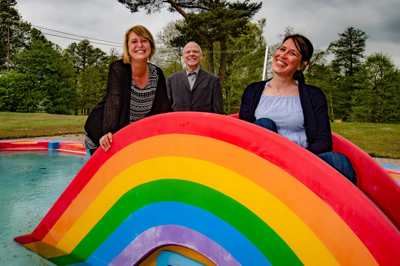 Drei Personen befinden sich in einem Freibad-Kinderbecken und lächeln in die Kamera. 