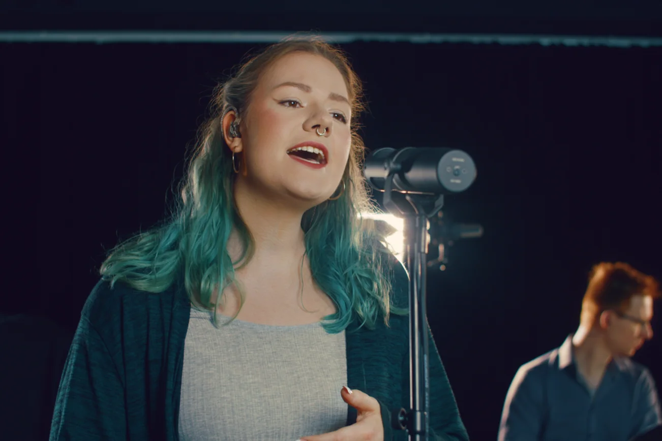 Junge Frau singt mit geschlossenen Augen in ein Mikrofon.