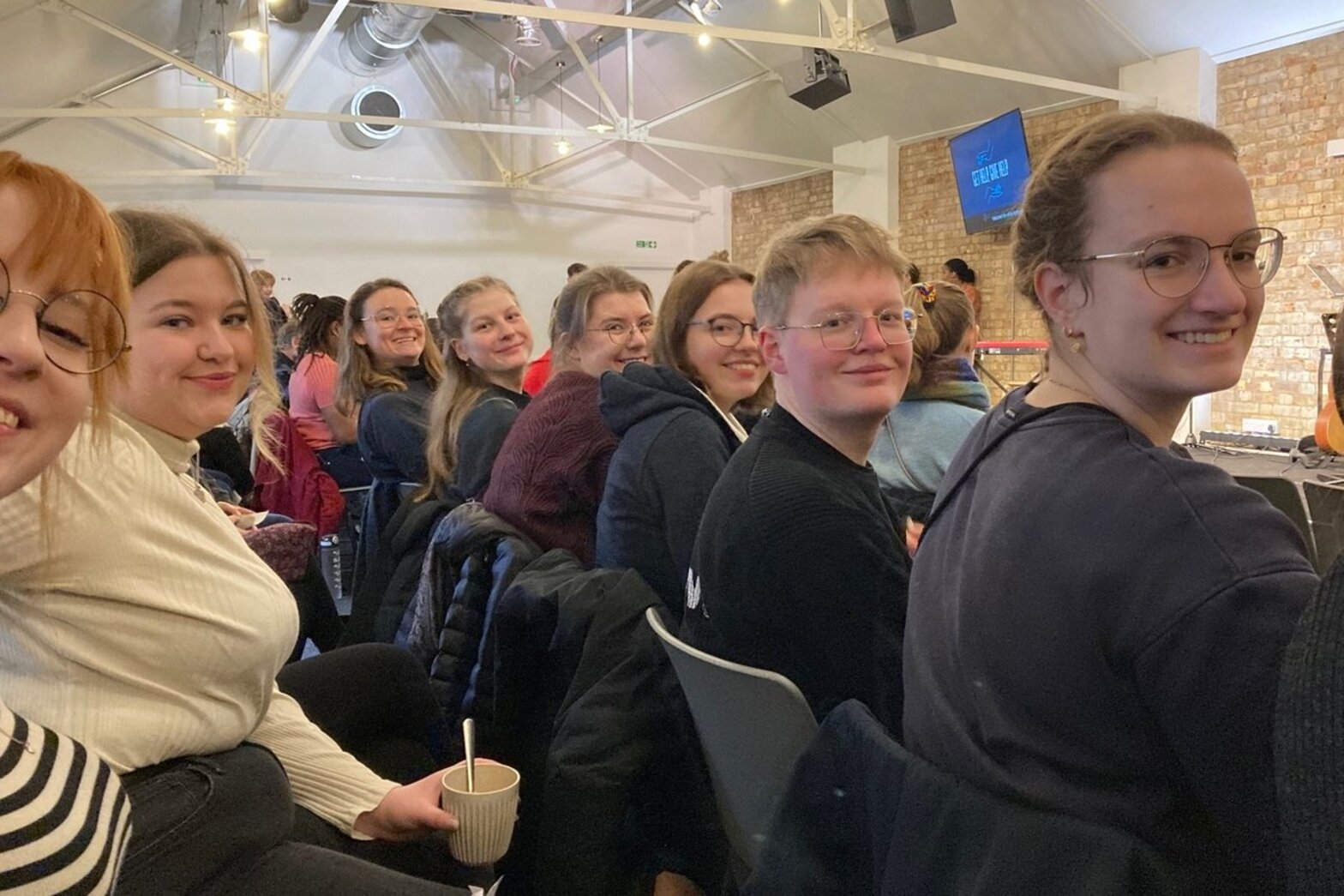 Junge Menschen sitzen in einem hellen Raum und drehen sich zur Kamera.