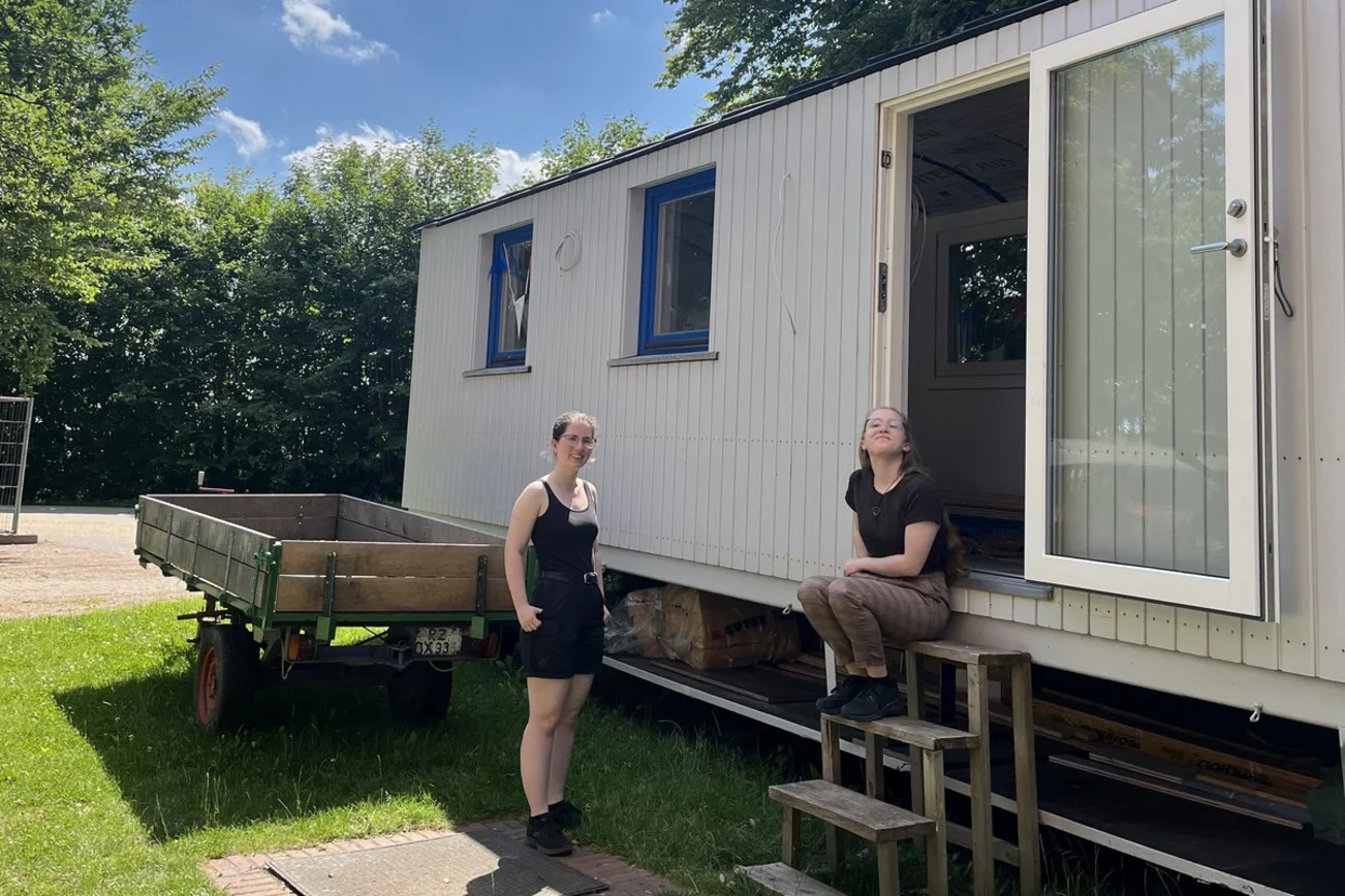 Zwei Frauen stehen vor einem weißen Zirkuswagen.