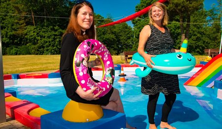 Zwei Frauen stehen an einem Schwimmbecken mit Badetieren und lächeln in die Kamera. 