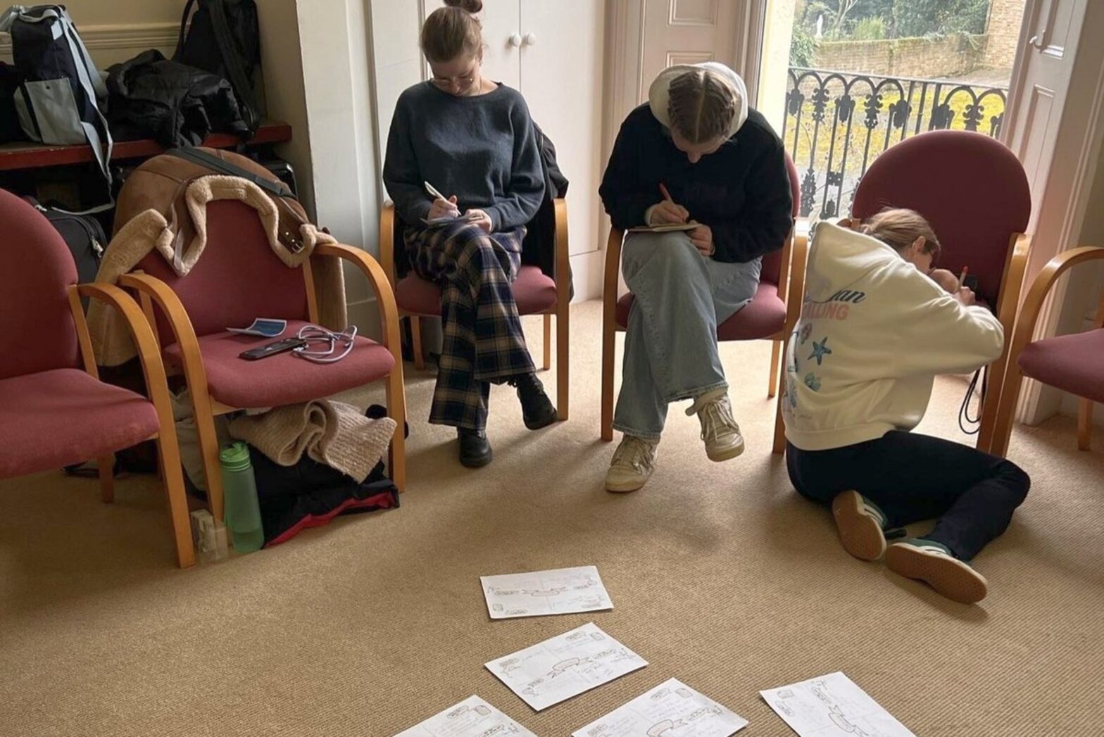 Drei junge Menschen in einem Stuhlkreis schreiben etwas auf Papier.