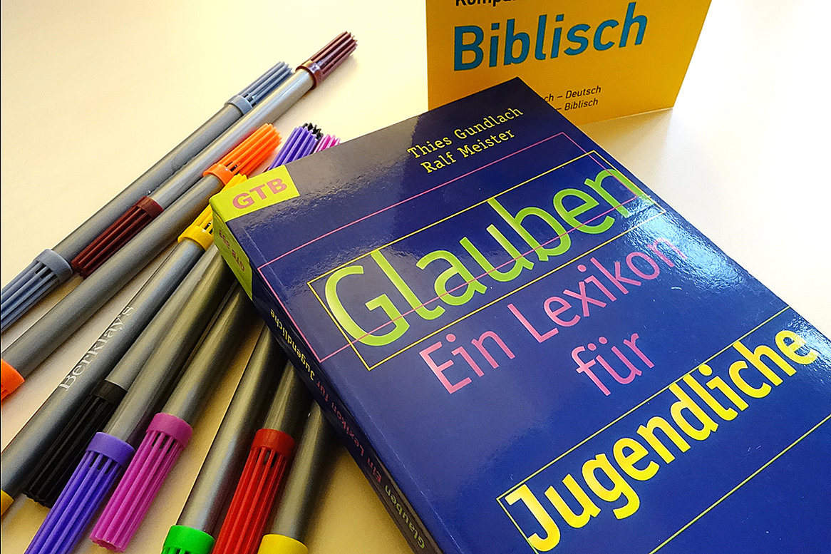 Buch "Glauben - Ein Lexikon für Jugendliche" liegt auf mehreren bunten Filzstiften