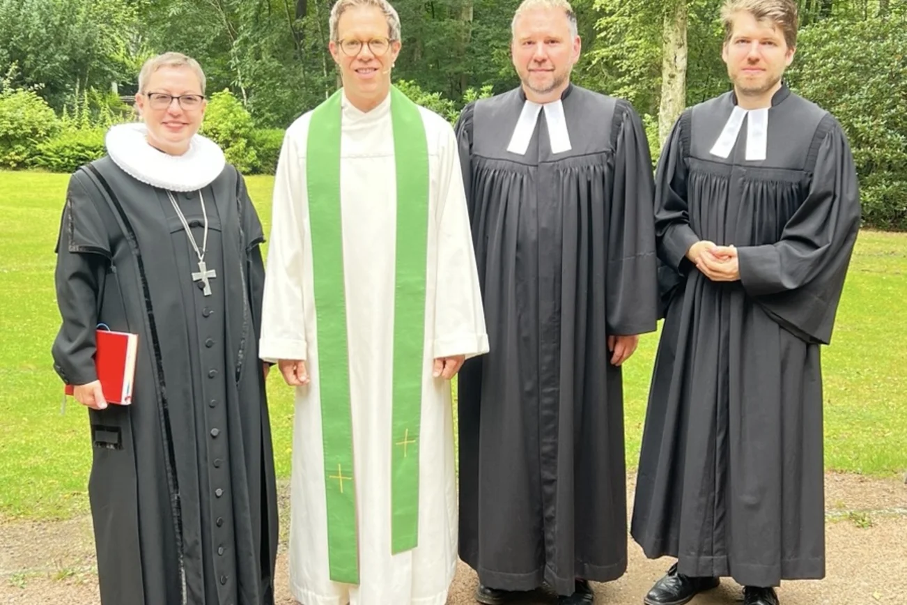 Vier Personen stehen unter freiem Himmel und lächeln in die Kamera. 