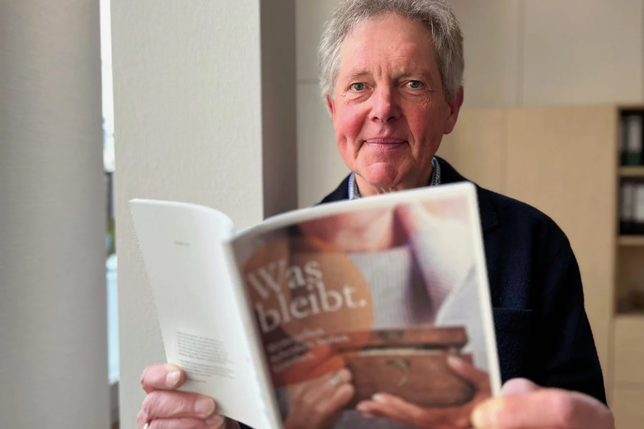 Ein Mann hält eine Broschüre in den Händen und blickt in die Kamera.