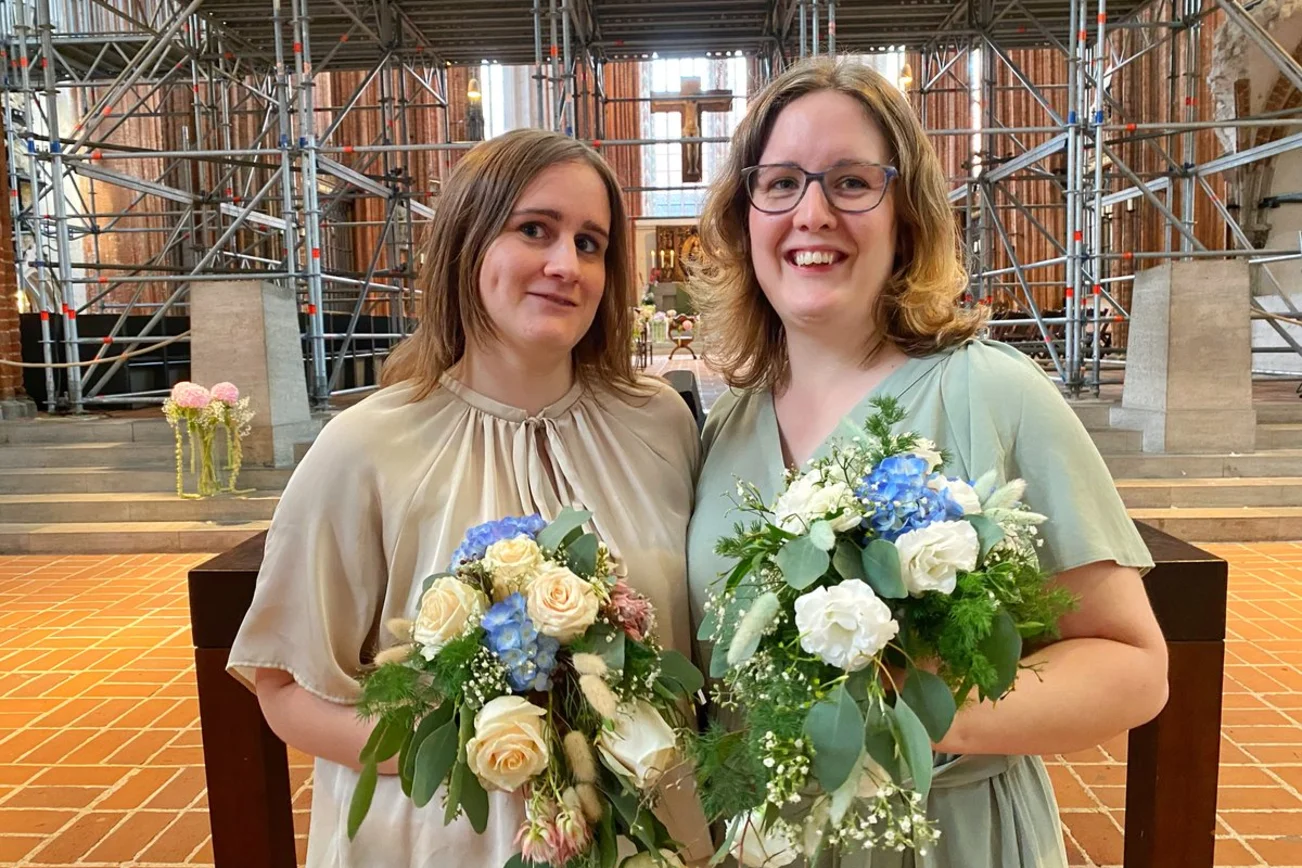 Zwei festlich gekleidete Frauen vor einer Kirche. 