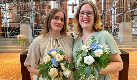 Zwei festlich gekleidete Frauen vor einer Kirche. 