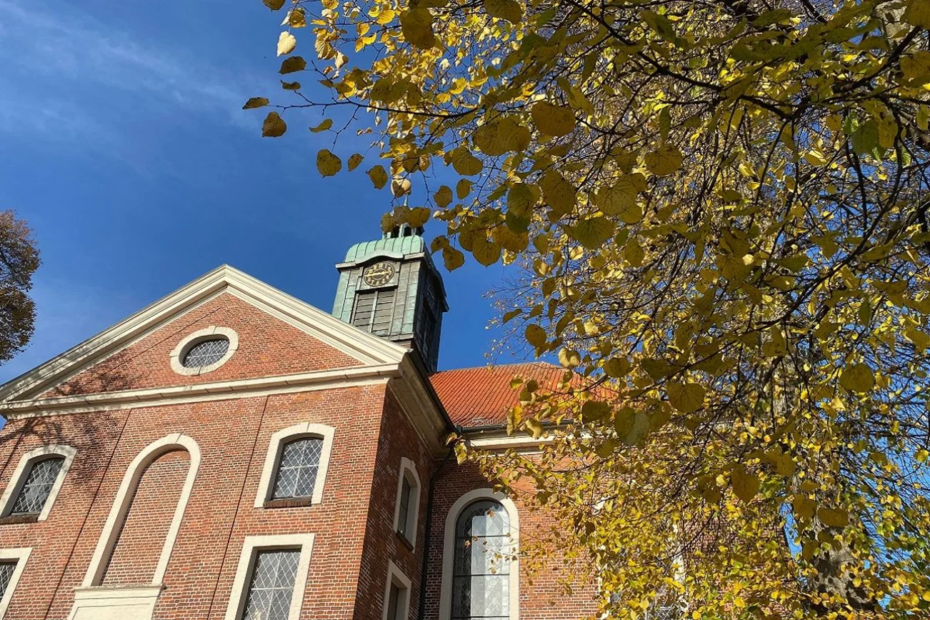 Kirche vor blauem Himmel und herbstlichem Laub. 