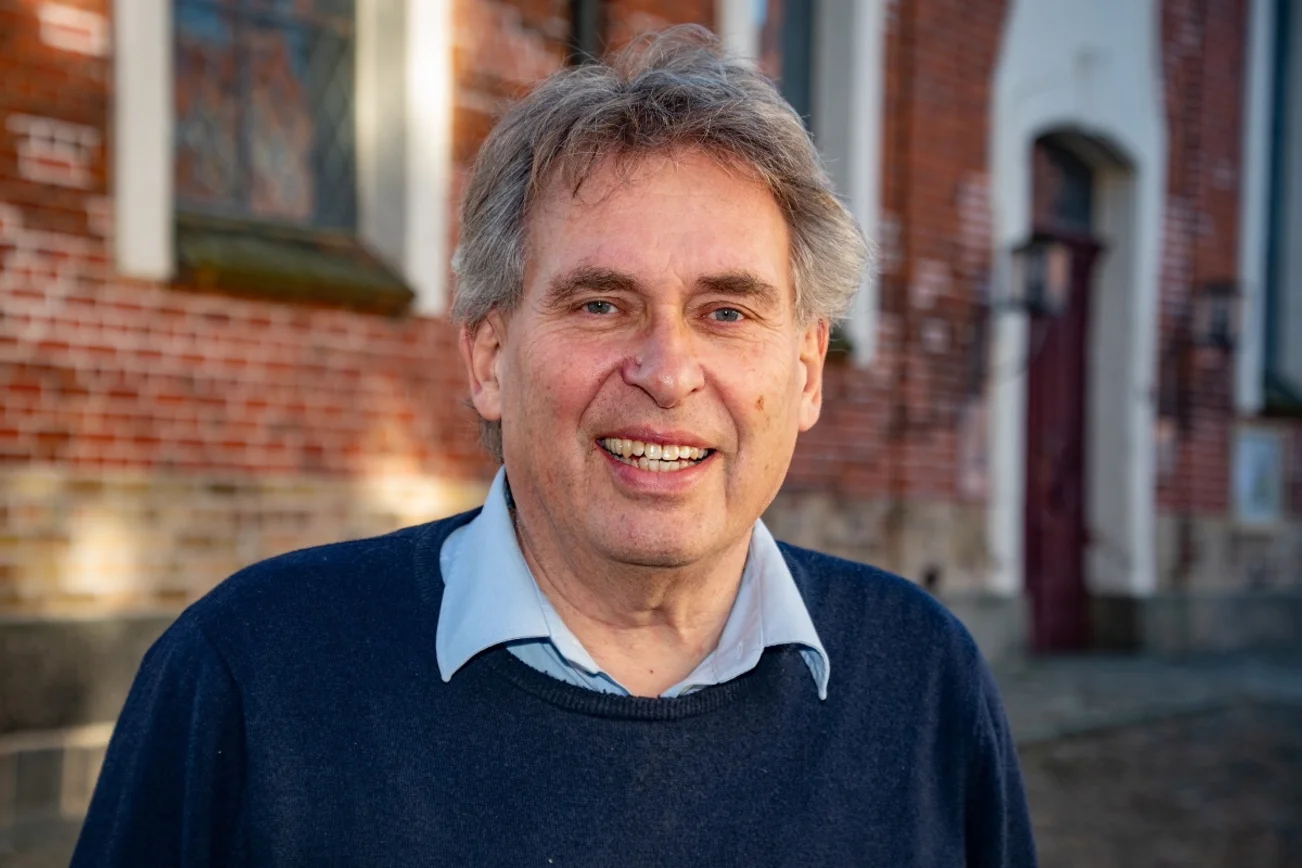 Ein Mann schaut freundlich lächelnd in die Kamera. Im Hintergrund die Ratzeburger Petrikirche.