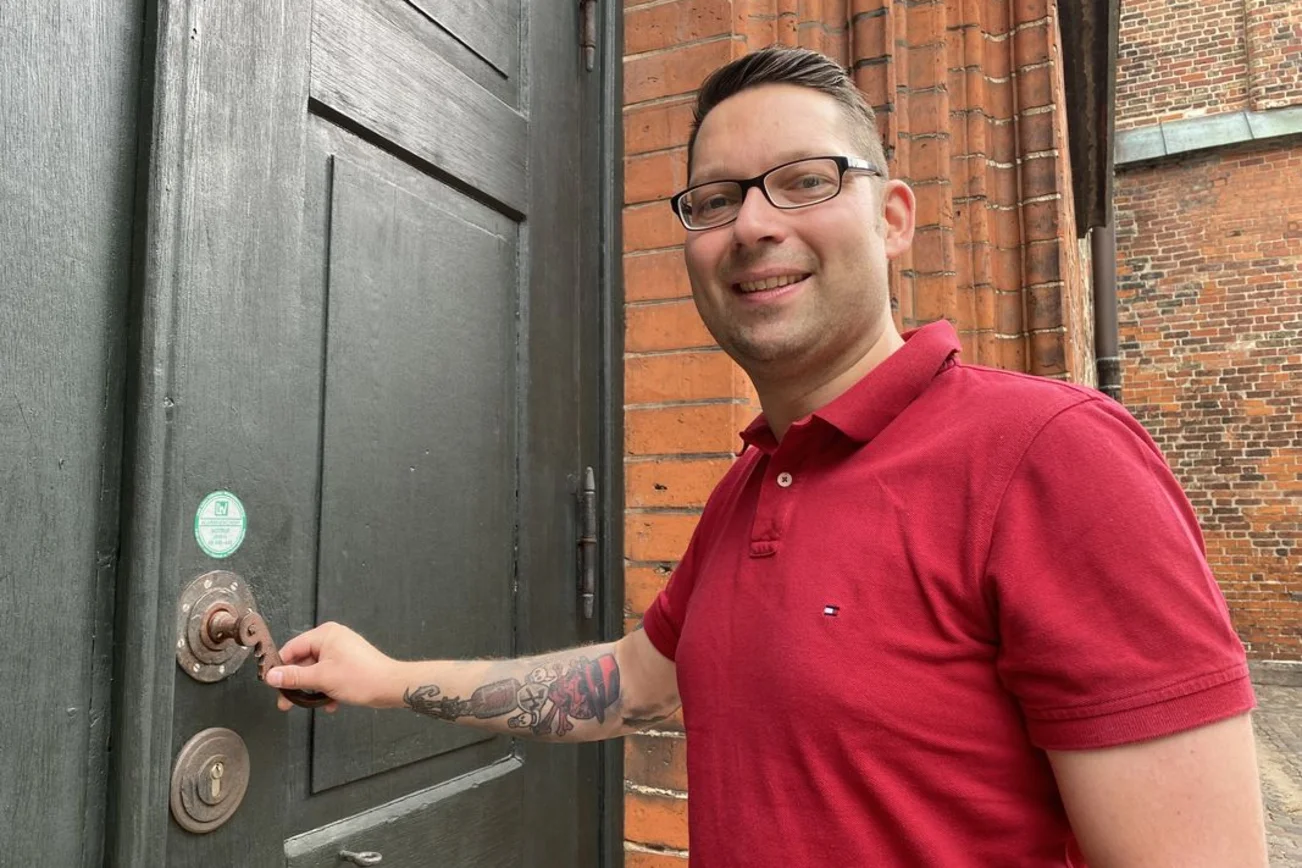 Mann im roten T-Shirt öffnet eine Kirchentür