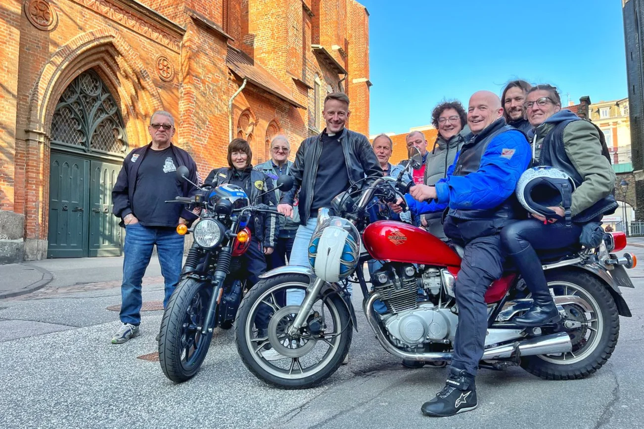 Eine Gruppe Menschen stehen mit zwei Motorrädern vor einer Kirche. 