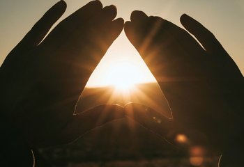 Zwei Hände formen ein Dreieick, durch dass die Sonne scheint. - Copyright: Unsplash (Nathan Dumla)