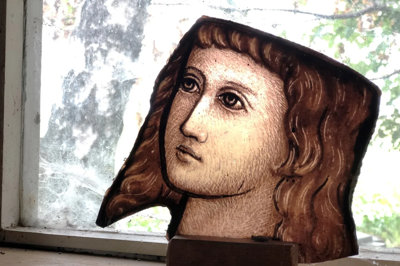 Eine Bruchstück eines Kirchenfensters. Darauf ein Gesicht im Halbprofil.