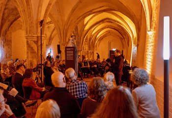 Blick in einen erleuchteten räum, in dem Menschen sitzen.  - Copyright: Oliver Beck