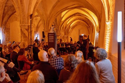 Blick in einen erleuchteten räum, in dem Menschen sitzen.  - Copyright: Oliver Beck