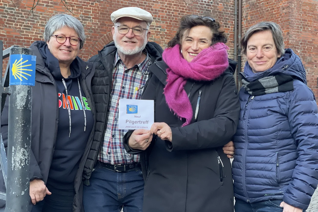 Ein Mann und drei Frauen stehen vor einer Backsteinkirche.