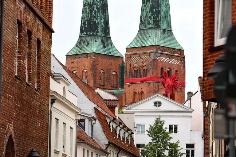 Die beiden Türme vom Dom zu Lübeck im Hintergrund, der rechte Turm ist mit einer roten Schleife versehen. Im Vordergrund die Fassaden von Innenstadthäusern