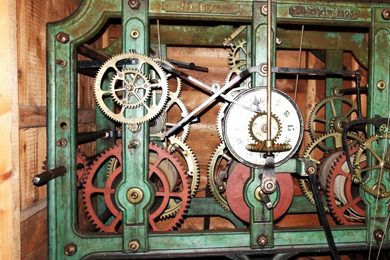 Der Blick in das hölzerne Gehäuse des Uhrwerks. Zu sehen sind Zahnräder unterschiedlicher Größe, die ineinander greifen.