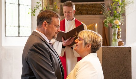 Ein Paar steht vor einem Pastor und blickt sich gegenseitig an. 