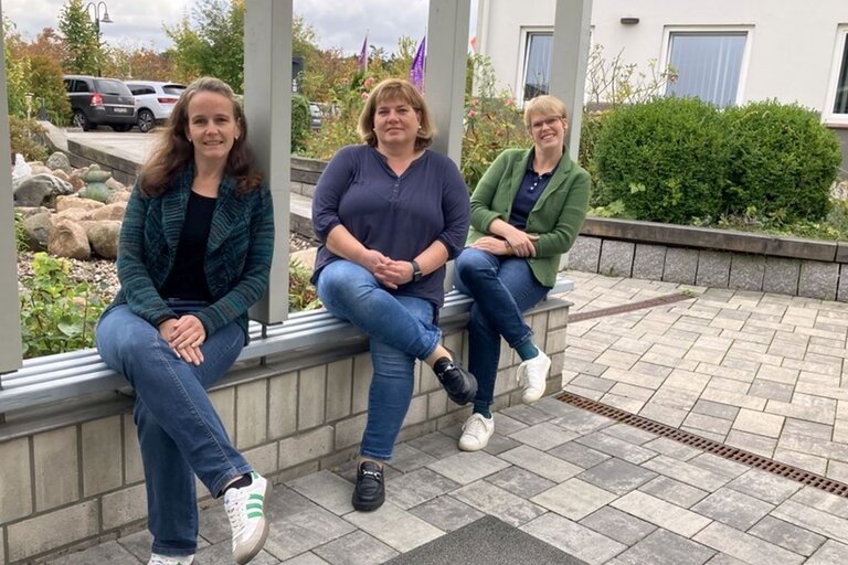 Drei Frauen sitzen auf einer kleinen Mauer.