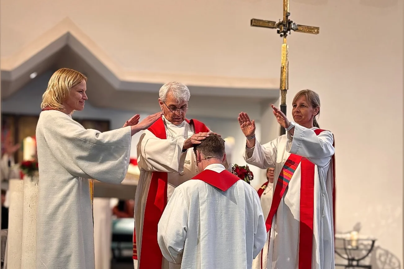 Mehrere Pastoren segnen einen knieenden Pastor in einer Kirche.