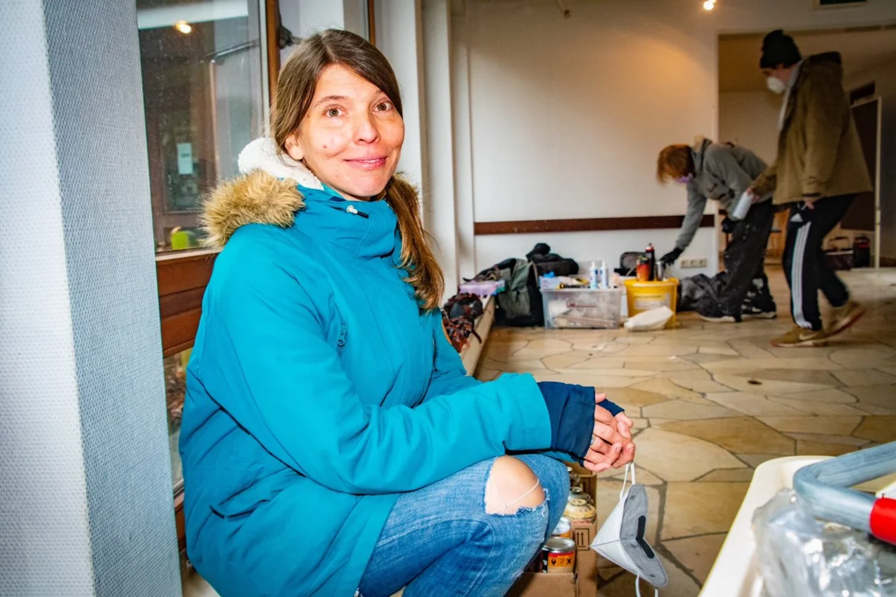 Eine Frau hockt in einem Raum und lächelt in die Kamera. 