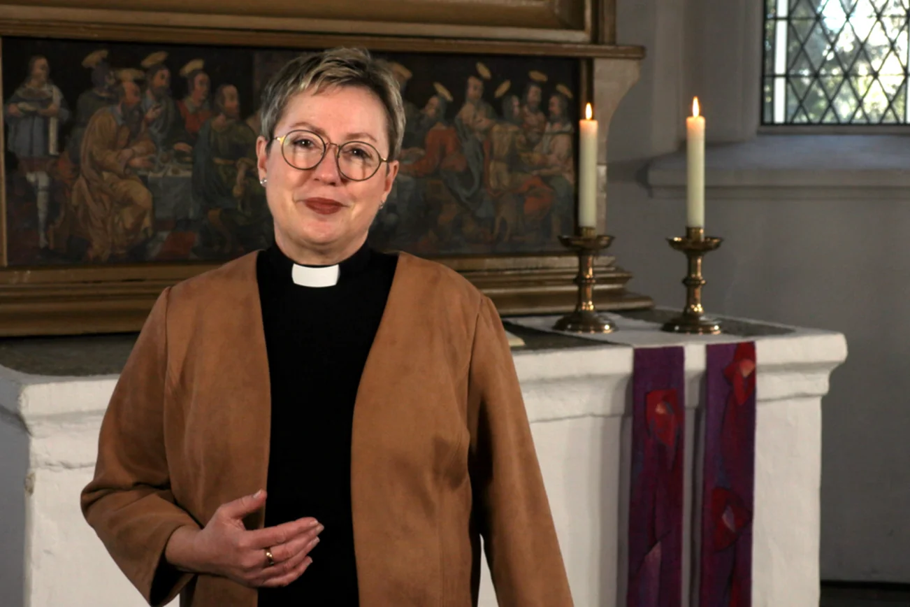Eine Frau steht in einer Kirche und lächelt in die Kamera. 