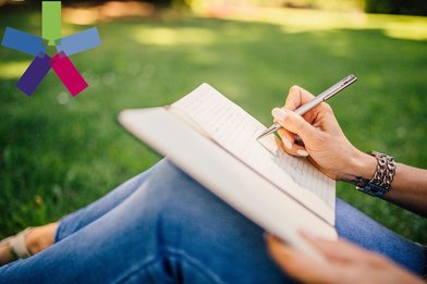 Frau sitzt im Gras mit Schreibheft und Stift in der Hand - Copyright: StockSnap|pixabay