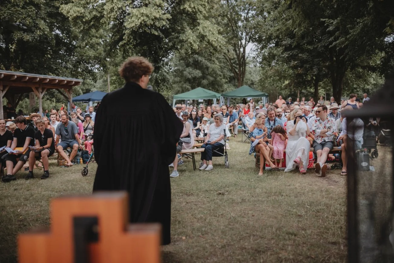 Blick auf einen schwarz gekleideten Pastor, der vor einer Menschenmenge spricht.