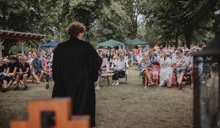 Blick auf einen schwarz gekleideten Pastor, der vor einer Menschenmenge spricht.