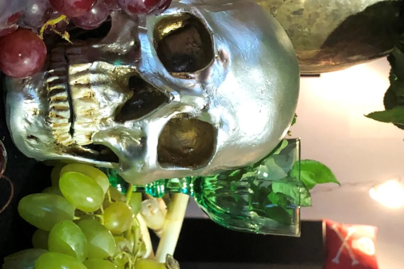 Ein silberfarbener Totenschädel liegt zwischen grünen und blauen Weintrauben.