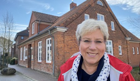 Eine Frau steht lächelnd vor einem Haus. 