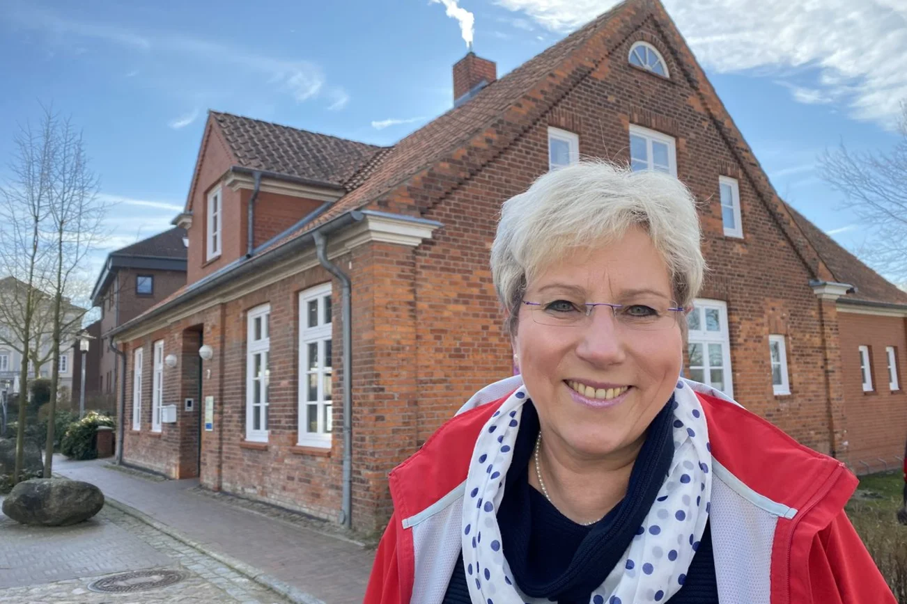 Eine Frau steht lächelnd vor einem Haus. 